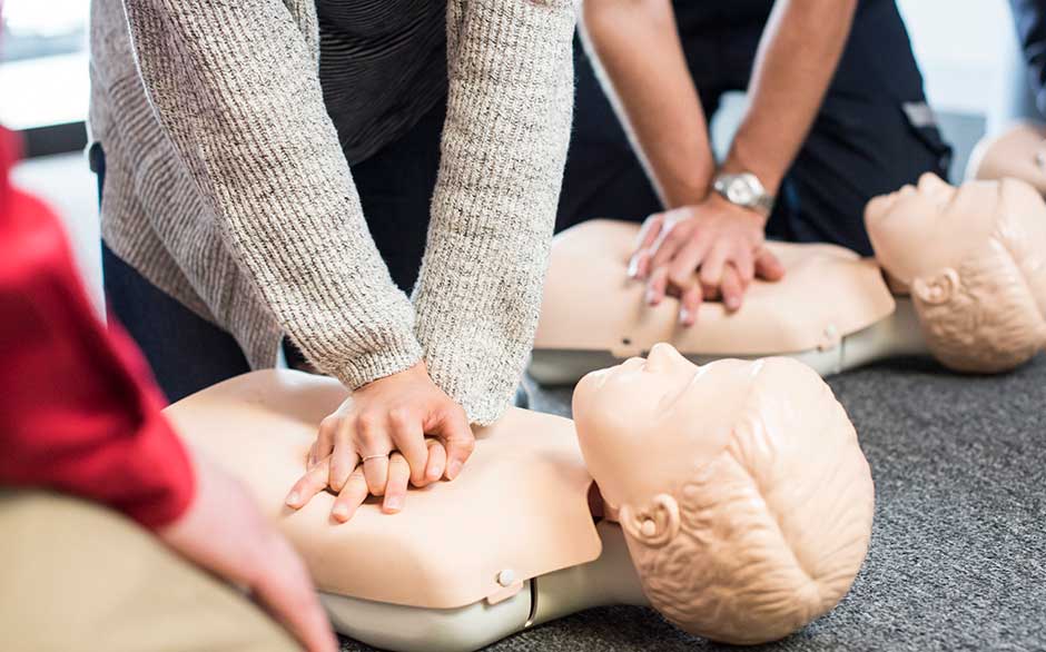 Hands performing CPR in CPR class students practicing CPR on manikin
