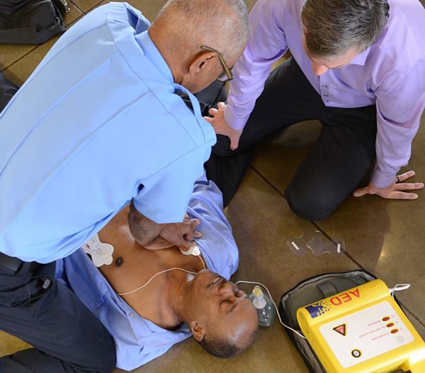 Paramedic using AED on man with bystander watching Implementing an AED